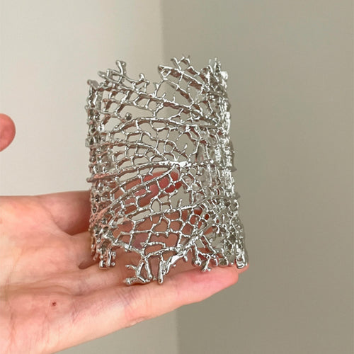 Silver coral lattice cuff held in palm showing openwork depth