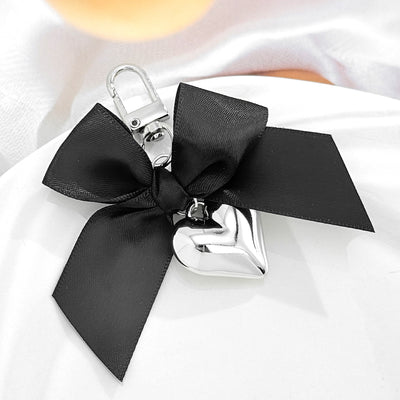 Black bow keychain with silver puffed heart on soft white fabric
