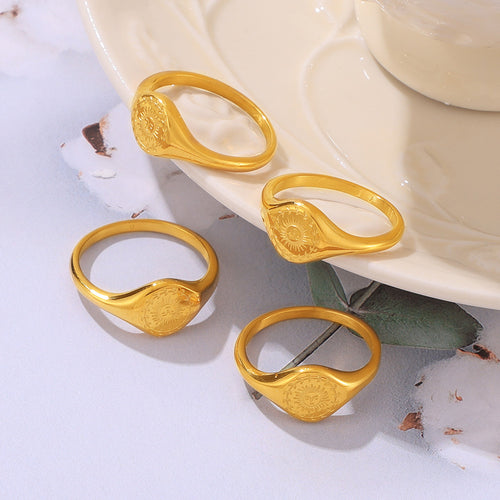 Four gold sun face signet rings on white surface near cup