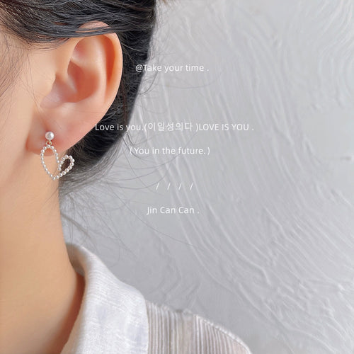Gold-tone white-pearl open-heart drop studs shown worn on an ear.