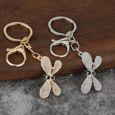 Silver-tone and gold-tone dragonfly keychains displayed together on wood and gray fabric.