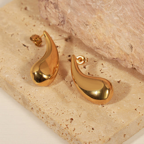 Pair of gold teardrop studs on beige stone surface