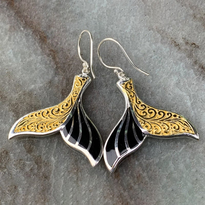 Pair of gold-and-black mermaid tail drop earrings on gray stone surface