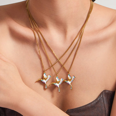 Three gold enamel hummingbird pendant necklaces layered on a collarbone