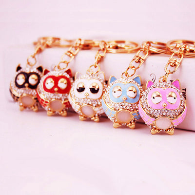 Five colored owl keychains are arranged in a row on a pink surface.