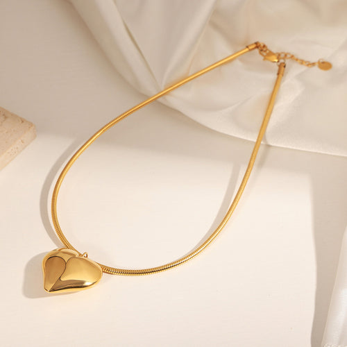 Gold puffy heart pendant snake chain necklace laid on white fabric