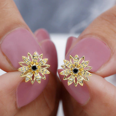 Gold daisy flower black center stud earrings held between fingers