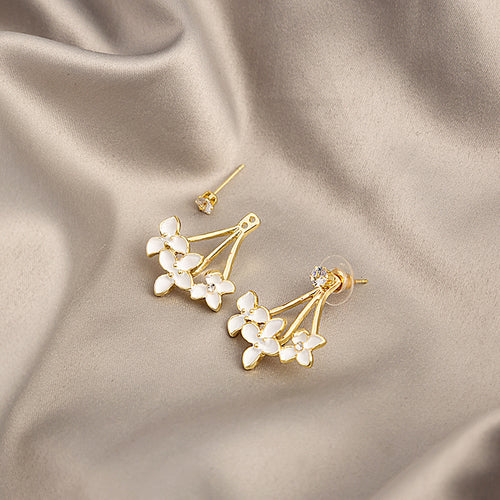 White enamel flower studs showing posts and plastic backs on satin cloth