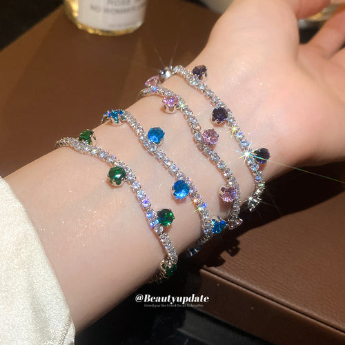 Three silver tennis bracelets with green blue and purple drops on wrist