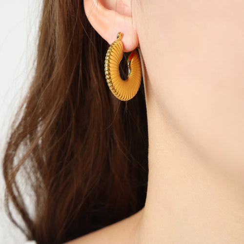 Gold ribbed fan hoop earring worn on ear close-up