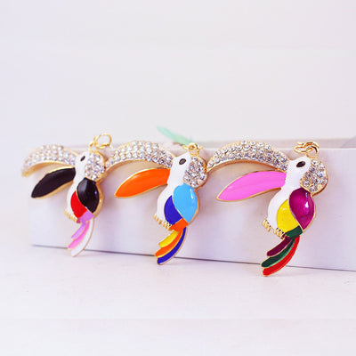 Three multicolor toucan charms with clear rhinestones and large curved beaks hang in a row.