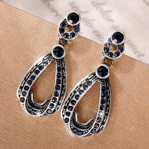 Silver dark blue pave teardrop drop studs on tan surface with paper backdrop