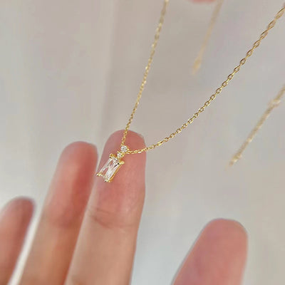 Gold baguette CZ pendant necklace held on fingertips close-up