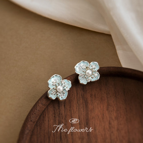 Pale aqua translucent flower and pearl stud earrings on a wood display.