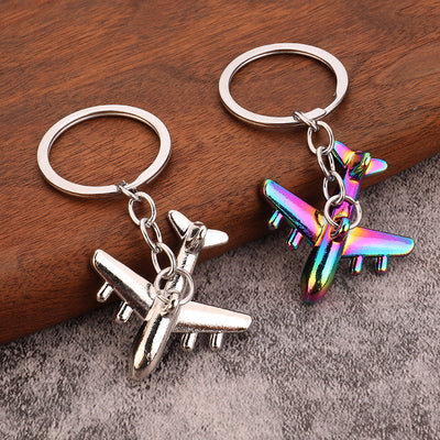 Two airplane keychains in silver-tone and iridescent finishes rest on a wooden surface.