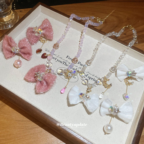 Pink and white fabric bow necklaces and stud earrings laid in wooden tray