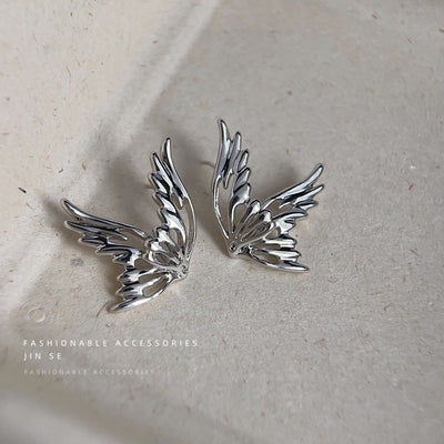 Silver hollow butterfly wing studs on beige stone surface