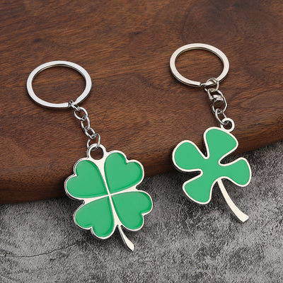 Two green four-leaf clover keychains with different leaf shapes rest on a wooden surface.
