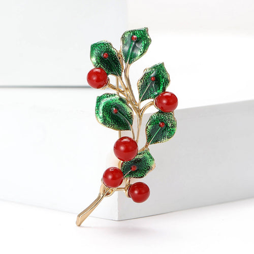 A slim gold tone branch set with red and green stones shown in a styled display.