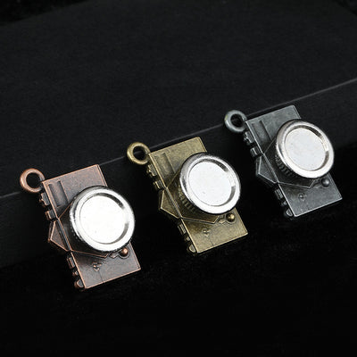 Three antique-finish camera charms in copper, bronze and gunmetal arranged on a dark cloth