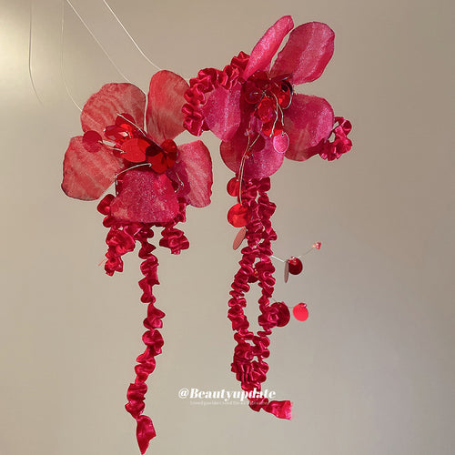 red fabric flower clip earrings with beaded fringe shown in an on-ear styling view
