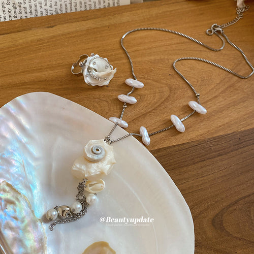 Shell spiral pearl necklace and rose ring on wooden table with shell dish