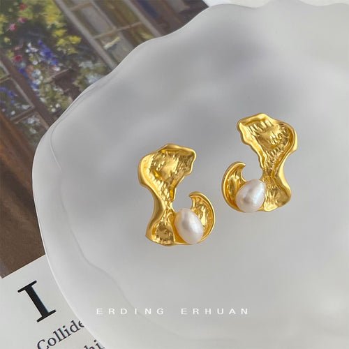 Close-up of gold organic metal pearl studs on white scalloped tray