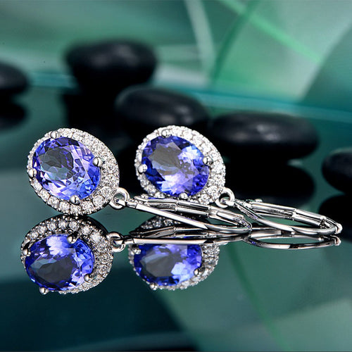 Pair of blue oval halo earrings lying on reflective glass