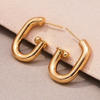 Gold U-shape hollow tube hoop earrings on beige fabric
