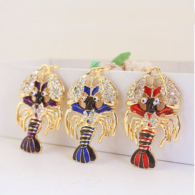 Three gold-tone lobster charms in purple, blue, and red are displayed together.