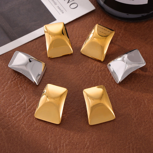 Gold and steel rectangular stud earrings arranged on brown leather
