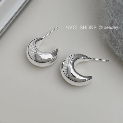 Silver hollow crescent half-hoop studs with posts on cream surface
