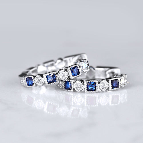 Angled detail view of silver tone hoop earrings with alternating blue and clear stones
