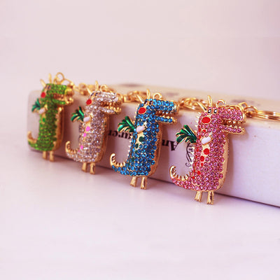 Four green, white, blue, and pink rhinestone dragon keychains displayed against a pale box.
