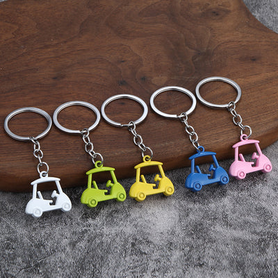 Five golf cart keychains in white, green, yellow, blue, and pink displayed on wood and gray fabric.