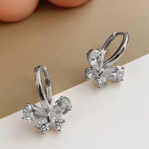 White metal butterfly huggie hoops on two-tone surface