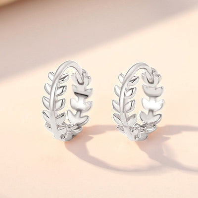 Pair silver leaf laurel hoop earrings standing on peach surface