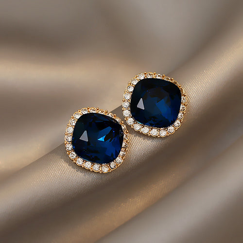 Deep blue faceted square centers in textured gold-tone frames shown in a front product view