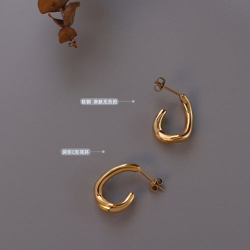 Pair of gold irregular C-shape studs flat lay with titanium labels