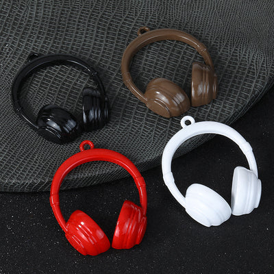 Four glossy headphone-shaped charms in black, red, white and coffee brown on a gray textured fabric