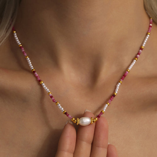 Close-up of pink stone shell bead necklace with center pearl on collarbone