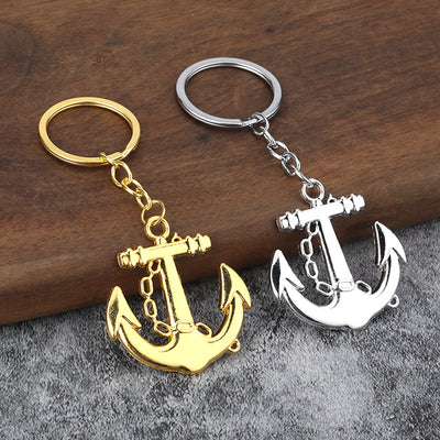 Gold-tone and silver-tone anchor keychains displayed together on wood and gray fabric.