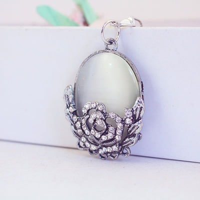 Close-up front view of a gray oval cabochon in a silver-tone rose frame with clear accents.