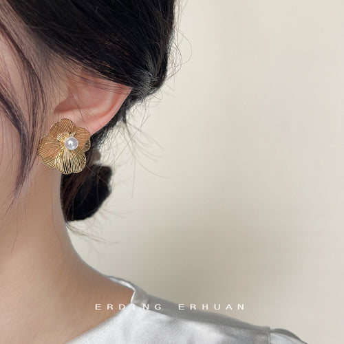 Gold openwork flower pearl stud worn on ear close-up