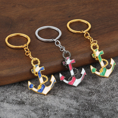 Three blue, pink, and green anchor keychains rest on a wooden and gray surface.