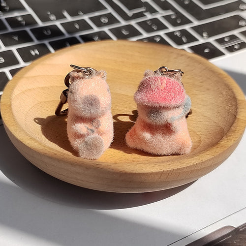 Two peach flocked capybara keychains with wood fish and pink headphones on wooden dish