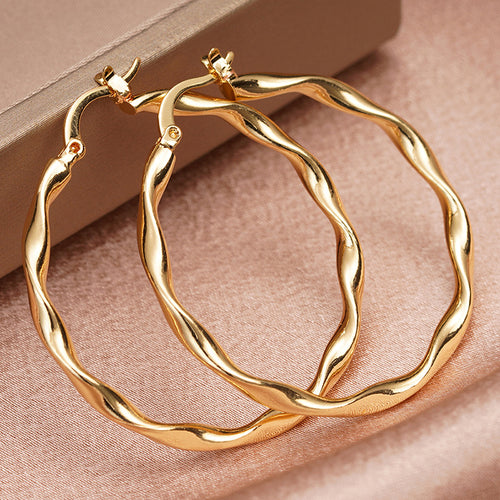 Gold twisted wavy thin hoop earrings pair on pink satin with beige box