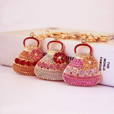 Three rhinestone handbag keychains displayed in pink, white, and peach colorways.