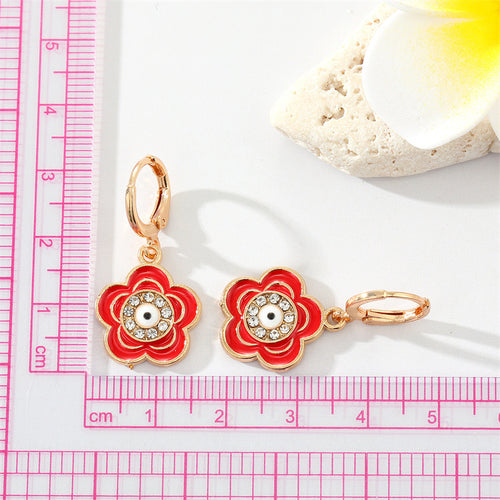 Red enamel flower evil eye hoop earrings beside pink ruler and plumeria