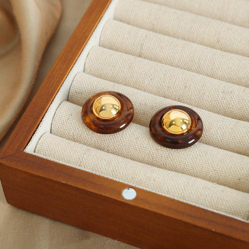 Pair of amber resin gold-dome studs on beige jewelry tray